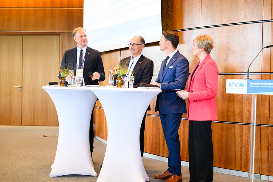 An zwei Stehtischen sind zu sehen: Viktors Valainis, Wirtschaftsminister der Republik Lettland, Dr. Wolfgang Blank, Minister für Wirtschaft, Infrastruktur, Tourismus und Arbeit des Landes Mecklenburg-Vorpommern, Tom Scheffler, Vizepräsident der Industr An zwei Stehtischen sind zu sehen: Viktors Valainis, Wirtschaftsminister der Republik Lettland, Dr. Wolfgang Blank, Minister für Wirtschaft, Infrastruktur, Tourismus und Arbeit des Landes Mecklenburg-Vorpommern, Tom Scheffler, Vizepräsident der Industrie- und Handelskammer Rostock und Honorarkonsul der Republik Lettland in Mecklenburg-Vorpommern, Marianna Evenstein, Journalistin und Eventmoderatorin